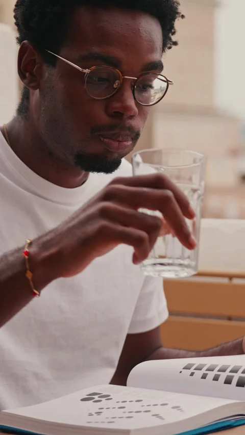 Young Man Reads Book And Drinks Water On Sunny Balcony Stock Footage 329936038