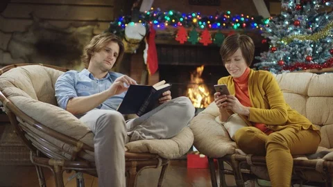Young man reads a book while his mother surfing the Internet on mobile phone in Stock Footage 100188444