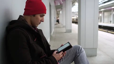 Young man reads e-book and waiting train in a subway station Stock Footage 68459626