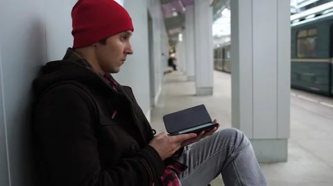 Young man reads e-book and waiting train in a subway station. Train arrives, he Stock Footage 68460319