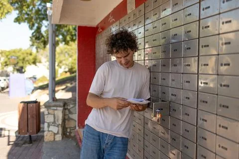 A young man reads a letter while standing at a mailbox. Stock Photos