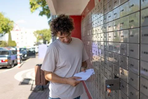 A young man reads a letter while standing at a mailbox. Stock Photos