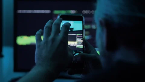 Young man recording data streams from computer monitors onto a smart phone Stock Footage 118976367