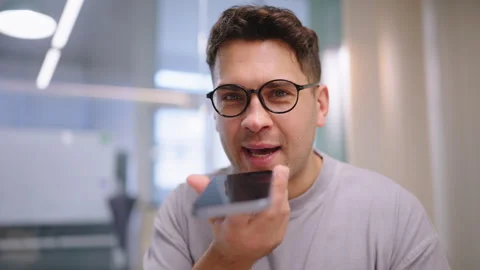 Young man recording voice message on smartphone in bright modern interior Video stock 324724772