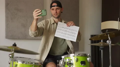 Young man records drum lesson on phone showing music sheet 스톡 동영상 201295707