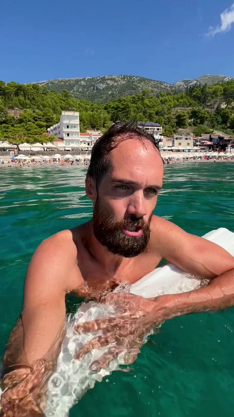 A young man records himself on video bathing in seawater on the background of th Stock Footage 251010400