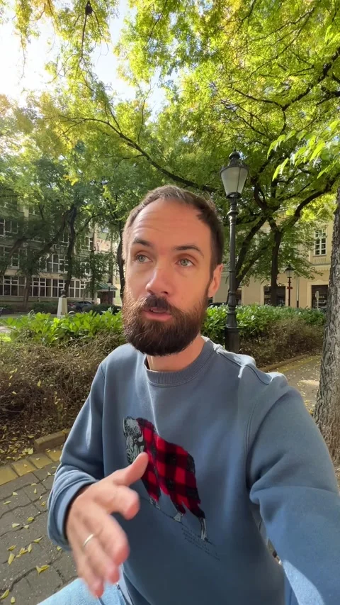 A young man records a video commentary while sitting in a city park Stock Footage 288117673