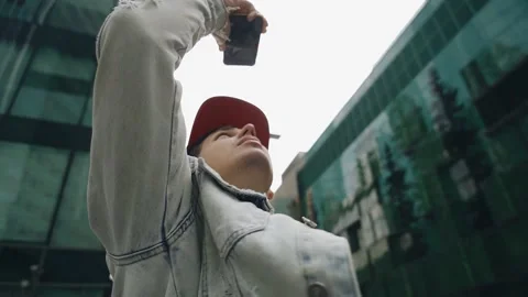 A young man in a red baseball cap takes pictures of himself on his phone Stock Footage 165603103