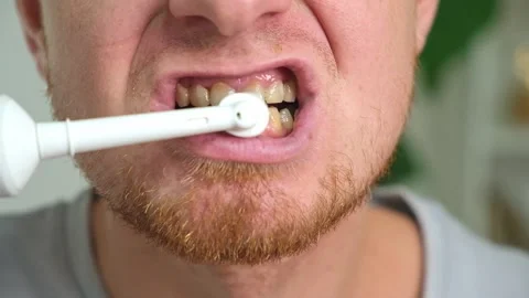A young man with a red beard is brushing his teeth with a white electric brush Stock Footage 218162414