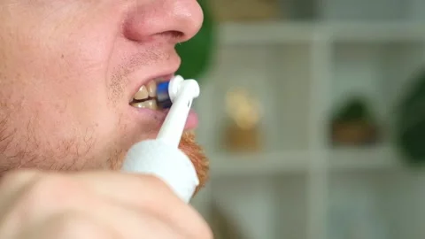 A young man with a red beard is brushing his teeth with a white electric brush Stock Footage 218162668