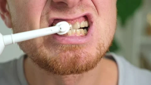 A young man with a red beard is brushing his teeth with a white electric brush Stock Footage 218614362