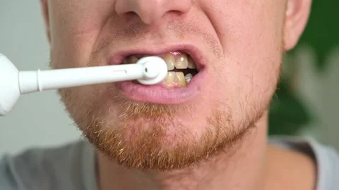 A young man with a red beard is brushing his teeth with a white electric brush Stock Footage 219751431