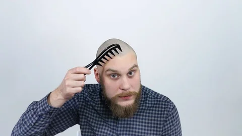 A young man with a red beard, combing his bald head with a large tooth comb. Stock Footage 122005475