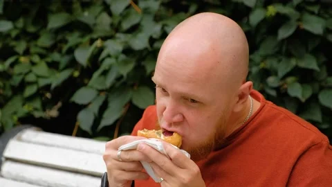 A young man with a red beard in the street eats a hamburger with appetite. Stock Footage 139110992