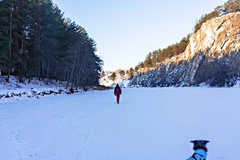 Young man in red clothes from back hiking with dog along snow covered river Stock Photos