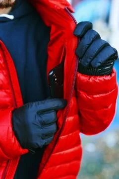 Young man in red down jacket puts phone in secret pocket, pocket for smartphone. Stock Photos