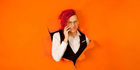 Young man with red dreadlocks speaking on smartphone and sticking out of hole Stock Photos