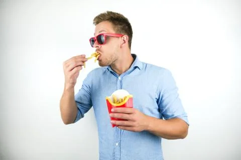 Young man in red eyeglasses eats french fries from fast food restaurant looks Stock Photos