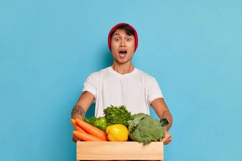 Young man in red hat and white tshirt holding box with vegetables in hands Stock Photos