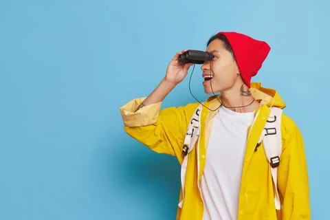Young man in red hat and yellow jacket with binoculars at his eyes looking for Stock-Fotos