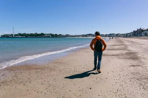 Young man in red jacket and jeans walking on Weymouth beach Stock Photos