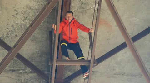 Young man in a red jacket climbs under the bridge support Stock Footage 34364139