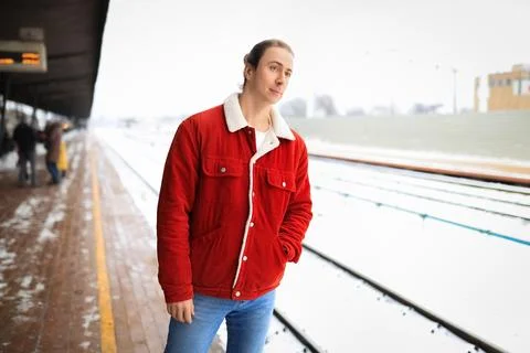 Young man in red jacket waiting on snowy train station platform during winter Stock Photos