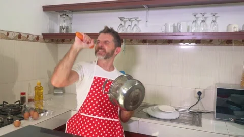 Young man in red kitchen apron singing and playing crazy holding carrot and pan Stock Footage 131803215
