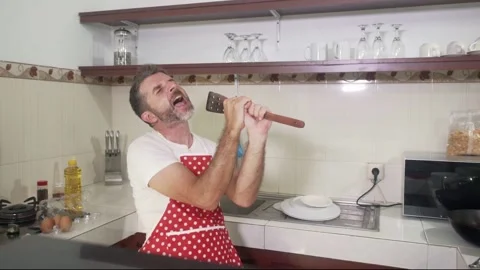 Young man in red kitchen apron singing crazy happy holding spoon Stock Footage 131803240