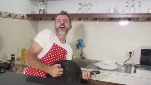 Young man in red kitchen apron singing and playing crazy holding pan Stock Footage 131803280