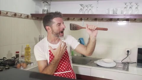 Young man in red kitchen apron singing crazy happy holding spoon Stock Footage 131803346