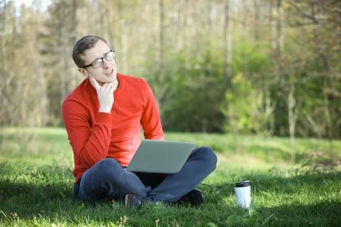 Young man in a red pullover with coffee cup and laptop working outside in a park Stock Photos