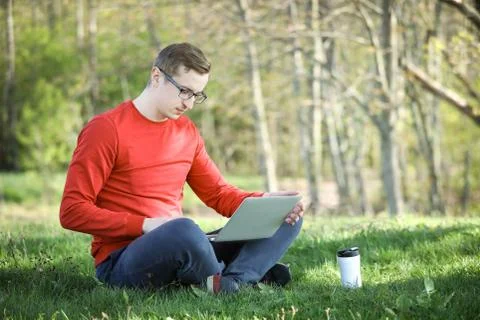Young man in a red pullover with coffee cup and laptop working outside in a park Stock Photos
