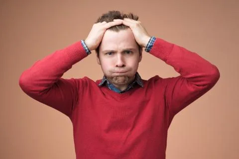 Young man in red sweater squeezing head with hands, suffering from stress Stock Photos