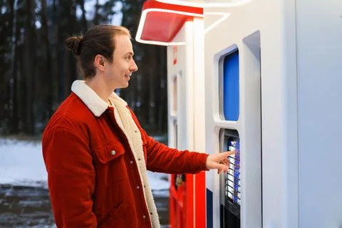 Young man in red winter jacket using outdoor vending machine kiosk in snowy.. Stock Photos