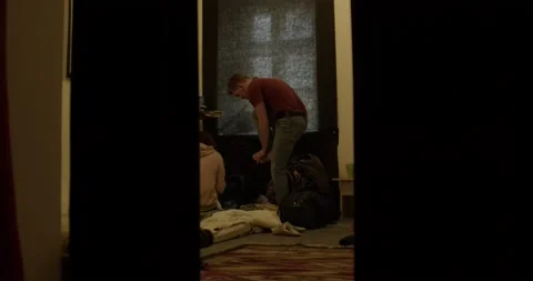Young man refugee puts on socks in gloomy room of shelter 스톡 동영상 172026880