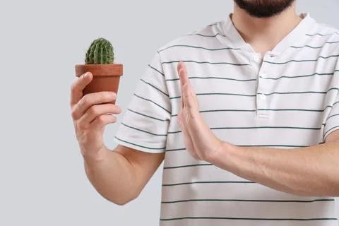 Young man rejecting cactus on light background. Hemorrhoids concept Stock Photos