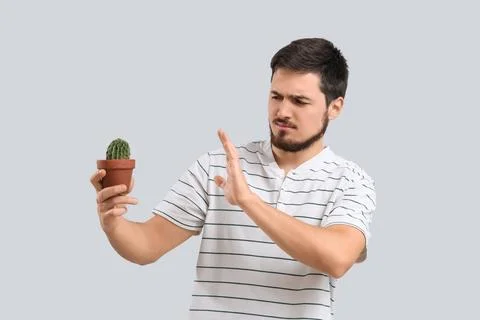 Young man rejecting cactus on light background. Hemorrhoids concept Stock Photos
