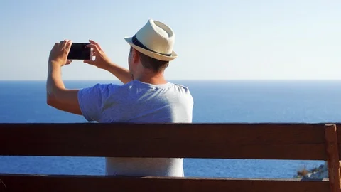 Young man relax on bench at edge of cliff take pictures on mobile phone. Man Stock Footage 103422357