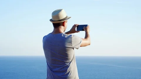 Young man relax at edge of cliff taking pictures on mobile phone. Male enjoying Stock Footage 99059381