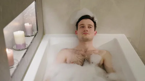 A young man relaxes in a bubble bath, leaning back with a calm expression Stock Footage 304811192