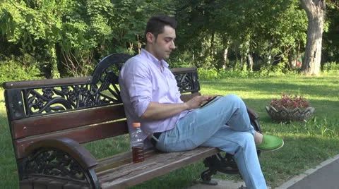 Young man  is relaxes in the park ,using touchscreen tablet Vídeos de archivo 25554474
