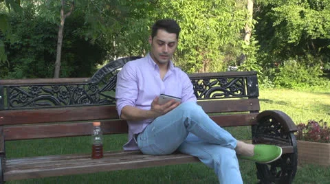 Young man  is relaxes in the park ,using touchscreen tablet Vídeos de archivo 25555413