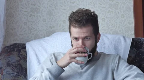 Young man relaxing and drinking coffee sitting on armchair at home Stock Footage 68753309