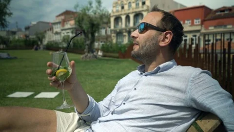 Young man relaxing and drinking cocktail in garden in cafe Stock Footage