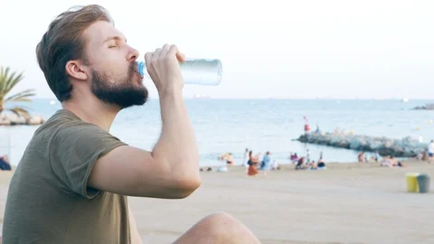 Young Man Relaxing and Drinking Water on Beach Stock Footage 118868946