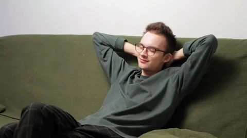 Young man relaxing on a couch with hands behind head and a content smile Stock-Footage 301520401