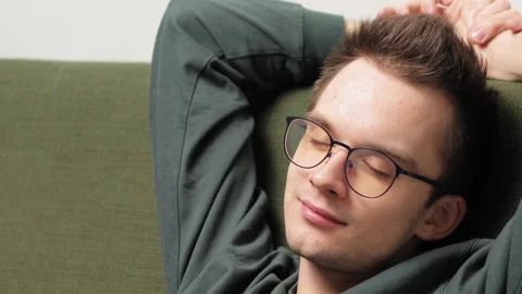 Young man relaxing on a couch with hands behind head and a content smile Stock Footage 301520523