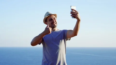 Young man relaxing at edge of cliff doing selfie on mobile phone. Male enjoying Stock Footage 99059604