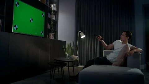 Young man relaxing on his sofa at night watching tv on his flat screen tv Stock Footage 100194557